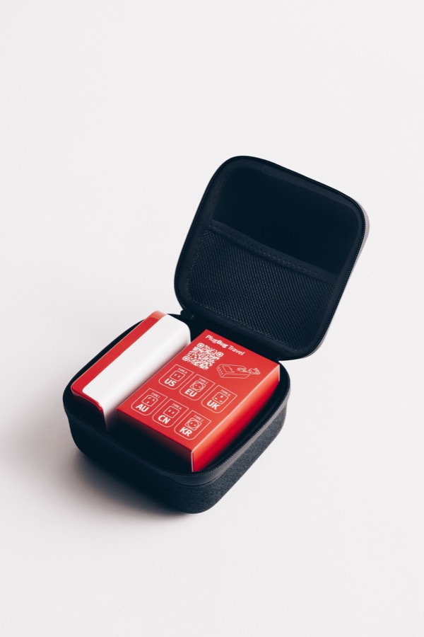 The PlugBug Travel zip case open, holding the charger and the red box of six international plugs